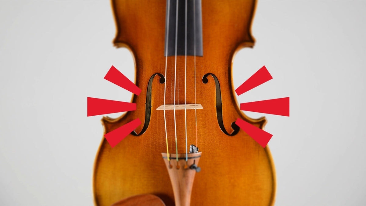 Close-up of a violin’s bridge between the f-holes, with red arrows pointing to both sides of the instrument