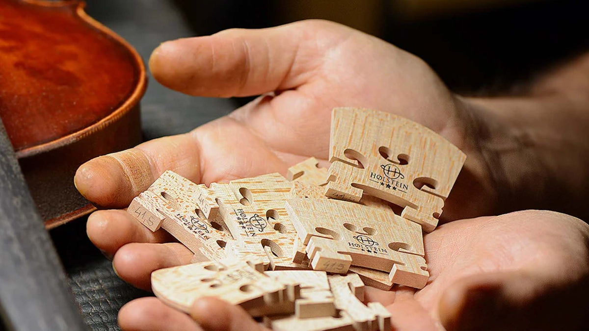 Luthier holding handcrafted Holstein violin bridges beside a violin