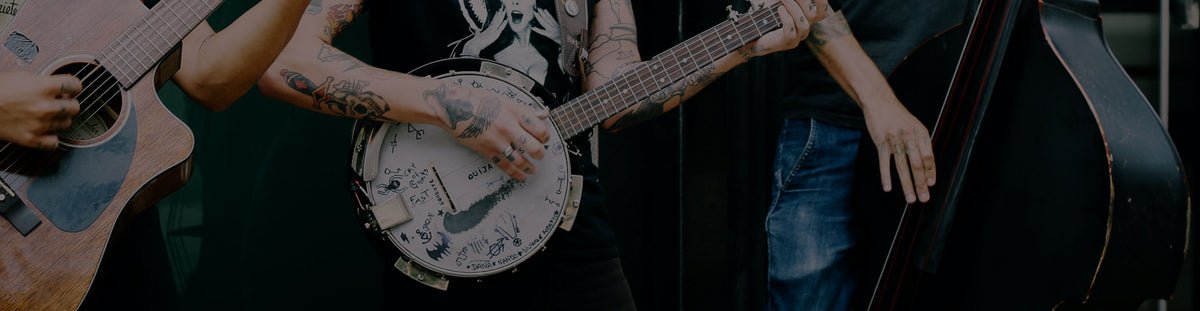 Close up of tattooed man strumming on banjo, next to band mates strumming on double bass and guitar