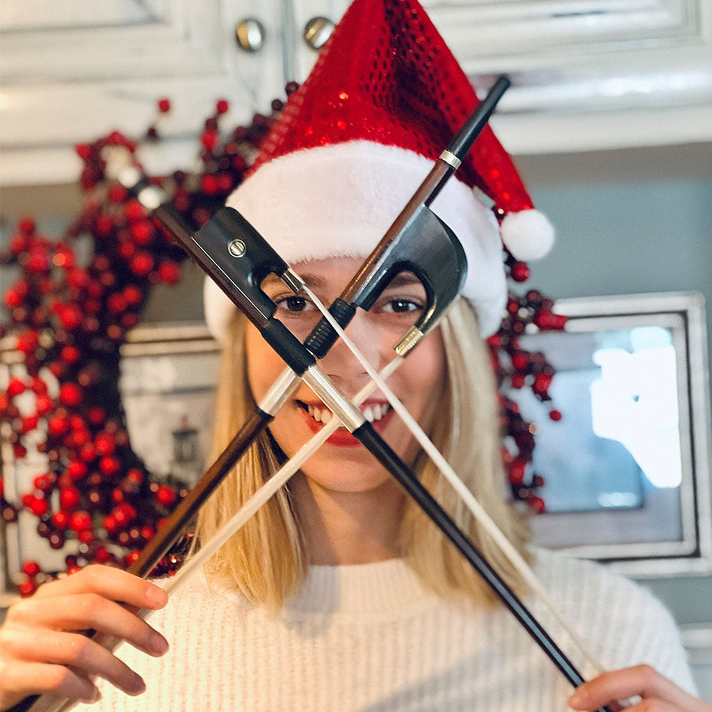 Christmas photo with a cello bow and double bass bow, held forming an X in front of the face of a player wearing a Santa hat
