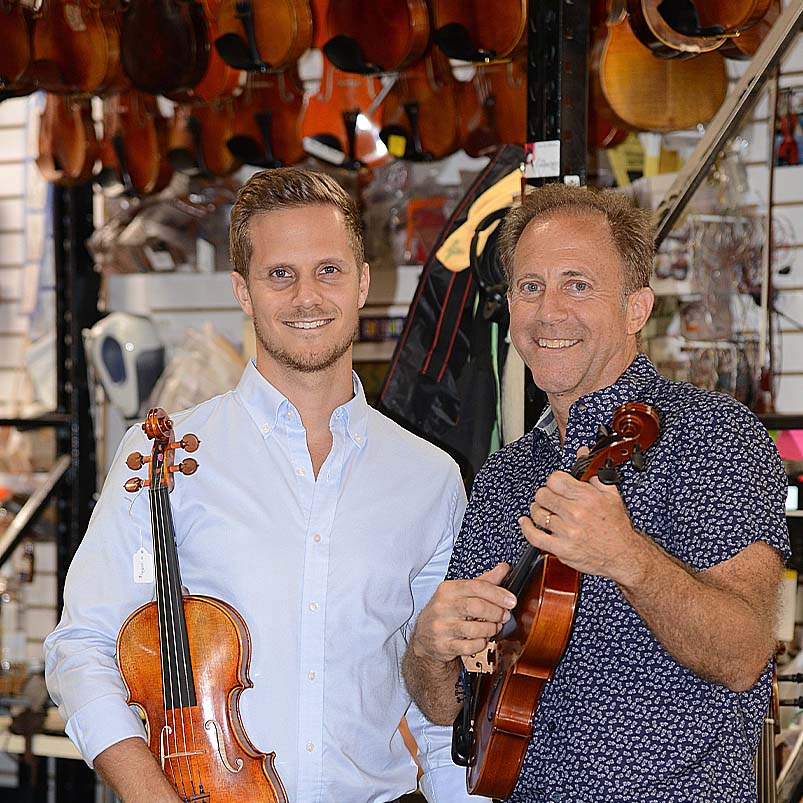 Fiddlershop founders, Michael Holstein and Pierre Holstein, posing in the Fiddlershop workshop with some of their favorite violin and violas for some of the best workshops